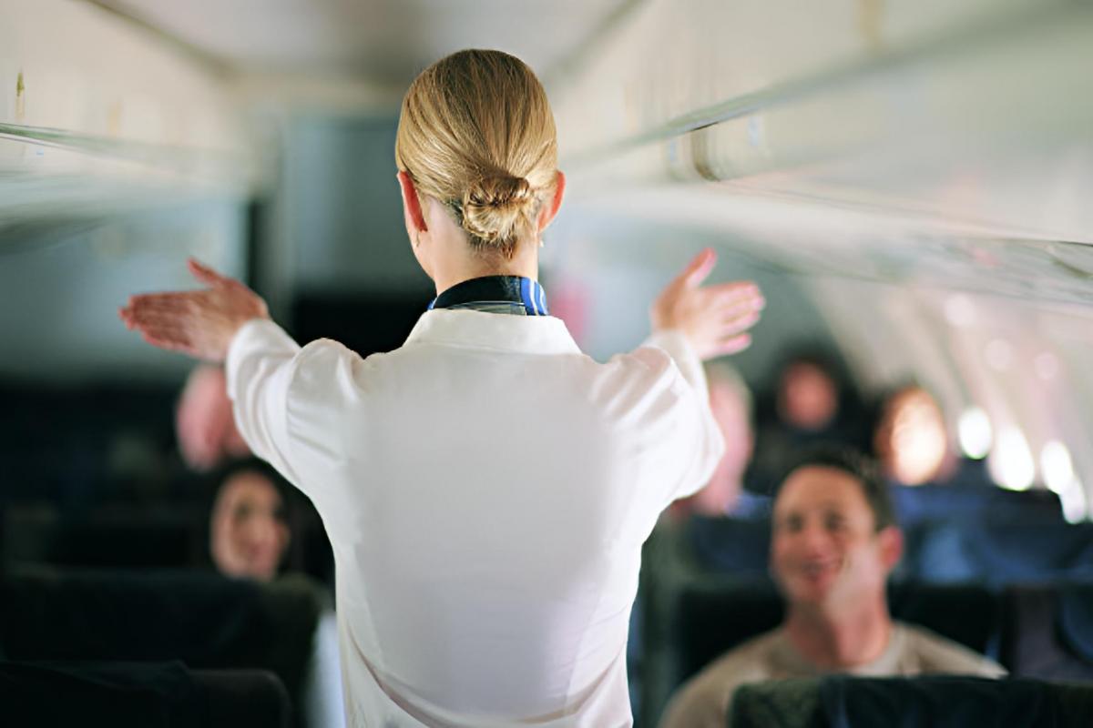 Vista trasera de una azafata explicando la seguridad del avión a los pasajeros