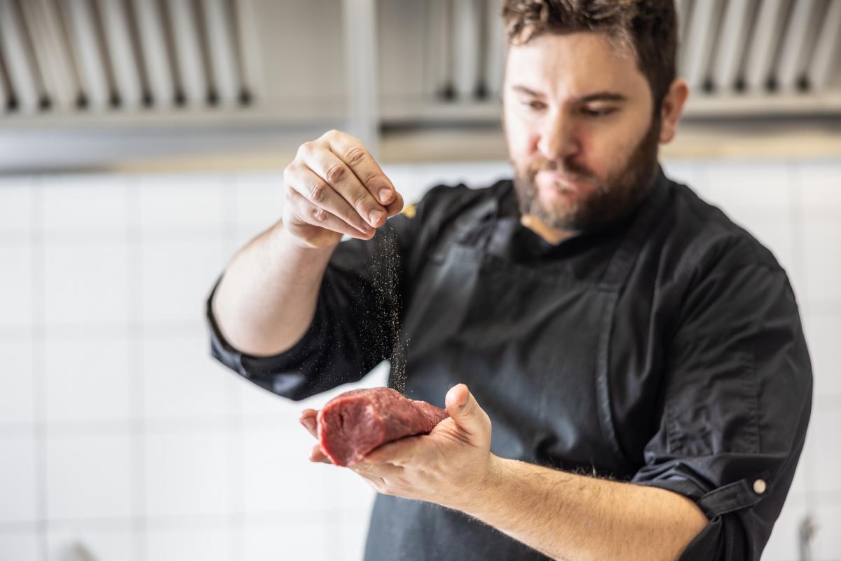 Un cocinero, echando la sal en un filete.