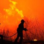 Dos bomberos intentan alcanzar el fuego con su manguera