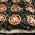 La masa se hace con harina, agua, aceite y margarina. Luego basta con recubrirla con espinacas rehogadas con cebolla y unas rodajas de tomate. Mira la receta en CookPad.