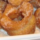 Con azúcar, zumo de naranja, aceite de oliva frito, cáscara de naranjas, raspaduras de limón, canela molida, levadura y harina. Consulta aquí la receta completa.