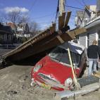 Foto del sábado 3 de noviembre del 2012 junto a un vehículo destrozado en el barrio neoyorquino de Rockaway por el huracán Sandy, que ha creado una carestía de automóviles de alquiler. (Foto AP/Kathy Willens)