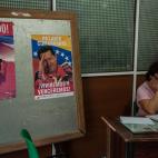 Una mujer en La Habana lee un documento con un mural con fotografías de Hugo Chávez.