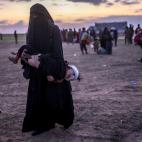 Una mujer completamente tapada, como impone el Estado Isl&aacute;mico, carga con un ni&ntilde;o herido, tras escapar de Baghouz.