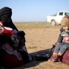 Una mujer completamente cubierta espera con su hijo a recibir ayuda tras salir de Baghouz.