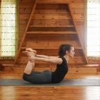 Túmbate boca abajo en la esterilla. Dobla las piernas y coge con las manos los pies por los empeines. Levanta del suelo la cabeza, el pecho y el abdomen al tiempo que tiras hacia arriba de los pies para levantar los muslos del suelo. Mantén la...