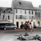 Turistas caminan por el lugar en el que yacía el cuerpo de un soldado alemán muerto en la plaza principal de Trevieres, Francia, después de la ciudad fuera tomada por las tropas estadounidenses que aterrizaron en la cercana playa de Omaha en 1944.