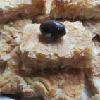 Se prepara con masa de hojaldre, jamón cocido, queso en lonchas, aceitunas verdes y negras, y huevos. Aquí tienes la receta completa.