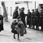 Dos refugiados llevan sus pocas posesiones en una bolsa mientras pasan frente a un grupo de soldados franceses.