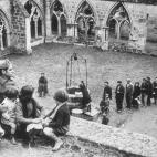 Un soldado se sienta con unos ni&ntilde;os mientras los refugiados espa&ntilde;oles hacen cola ante un pozo en una abad&iacute;a de Francia que serv&iacute;a de campo de refugiados entonces.