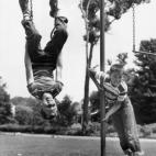 Sobre 1945: Un niño cuelga boca abajo en un columpio mientras otro se agarra a una barra. (Foto de Lambert/Getty Images)