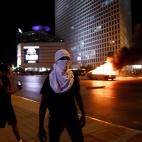 Un coche ardiendo y un manifestante enmascarado, en Tel Aviv.