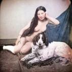 Una mujer desnuda sentada en el suelo, sólo con calcetines, al lado de un perro. Daguerrotipo estereoscópico coloreado a mano. 1850.