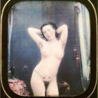 Una mujer desnuda, de pie al lado de una mesa, con hojas y flores pintadas en la cintura. Daguerrotipo estereoscópico coloreado a mano. 1850.