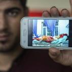 Un inmigrante iraquí muestra una fotografía en su teléfono móvil en la que, según dice, aparece él en la cama de un hospital tras un bombardeo, en la estación central de Stuttgart (Alemania).