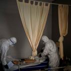 Con trajes de protecci&oacute;n para evitar infecciones, dos trabajadores de una funeraria preparan el cuerpo de un anciano fallecido por COVID-19 antes de retirarlo de un centro de mayores, en Barcelona, el 13 de noviembre de 2020.