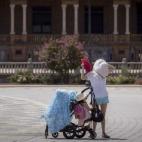 Una turista asiática acompañada de dos niños pequeños intenta aliviar el calor refrescándose con un abanico en la Plaza de España de Sevilla.