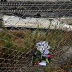 Un ramo de flores recuerda a las víctimas con la destrozada locomotora del tren al fondo