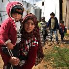 In this picture taken on Wednesday, March 12, 2014, a Syrian girl, foreground, carries her brother walks between tents with other children, background, on their way to a makeshift school at their refugee encampment in the Lebanese-Syrian border ...