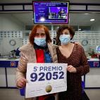La lotera Celia Pedreira (i) y una empleada de la administración de la avenida de Oza de A Coruña, posan con el cartel del quinto premio extraído en la Lotería de Navidad, del que han vendido una serie, diez décimos, del número 92.052.