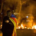 Un manifestante con m&aacute;scara y envuelto en una 'estelada' observa su tel&eacute;fono durante los disturbios.