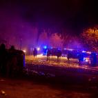 Los radicales se cubren tras un contenedor frente a los antidisturbios, en Barcelona.