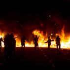 Siluetas de j&oacute;venes manifestantes con una barricada en llamas al fuego.