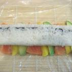 Colocamos sobre la línea hecha con aguacate, mango y salmón, el rollo de sushi y repetimos la acción de enrollar con la esterilla de bambú (cubierta de papel film) una vez más.