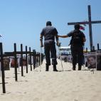 El oficial Alexsander Oliveira, herido por una granada mientras patrullaba una favela, camina con un amigo entre las cruces negras en la arena en honor a los 152 policías militares asesinados en Río de Janeiro en los últimos dos años.