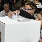 Dos niños echan el voto de su madre en la urna.