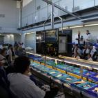 Los compradores, situados a ambos lados de las cintas, observan el g&eacute;nero antes de poner un precio a los pescados y mariscos.