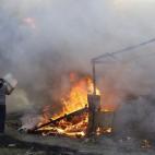 A man throws water on burning tents in a makeshift camp near Calais, France, Monday Feb. 29, 2016. Under the eye of hundreds of riot police, workers began pulling down tents and makeshift shelters in the sprawling camp in Calais on Monday, disma...