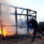 CALAIS, FRANCE - FEBRUARY 29: A migrant attempts to extinguish a fire as a hut burns as police officers clear part of the 'jungle' migrant camp on February 29, 2016 in Calais, France The French authorities have begun dismantling part of the mi...