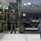 Una madre con su niño camina enfrente de militares rusos en Ucrania.