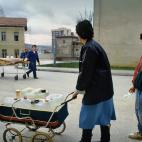 Una madre y su hija cargadas de bidones de agua que han llenado en una fuente p&uacute;blica observan el traslado al dep&oacute;sito de cad&aacute;veres de una persona v&iacute;ctima de un bombardeo. La vida, anclada en la m&aacute;s pura superv...