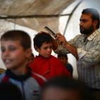 Un peluquero le corta el cabello a un niño sirio desde una tienda improvisada, en el campamento de refugiados Maiber al-Salam, cerca de la frontera turca, en la provincia siria de Aleppo (Haleb). (DIMITAR DILKOFF/AFP/Getty Images)