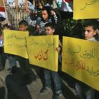 Niños y otros refugiados sirios que huyeron a Líbano por la violencia en su país sostienen pancartas que leen en árabe "La seguridad de los refugiados sirios es responsabilidad del gobierno libanés" (derecha) y "La comunidad internacional s...