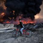 Un niño detiene su bicicleta al pasar por un yacimiento petrolífero incendiado por soldados del ISIS, en retirada tras la ofensiva de Mosul el 21 de octubre en Qayyarah (Irak).