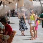 Unos turistas se refrescan con los difusores de vapor de agua de un bar de Sevilla.