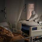 Trabajadores de una funeraria preparan el cuerpo de un fallecido por Covid, mientras su compa&ntilde;ero de habitaci&oacute;n en el asilo duerme, en Barcelona.