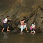 Una mujer acompaña a algunas estudiantes caminando por el agua en una playa camino de la escuela para ir a su primer día de clase en un pueblo al norte de Manila, Filipinas.