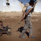 Un chico sirio tira de su hermano pequeño en un campo de refugiados sirios cerca de la frontera con Turquía.
