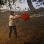 Una mujer con el rostro cubierto por una mascarilla arroja un cubo de agua hacia la maleza.