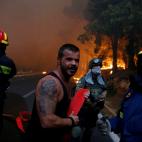 Bomberos, soldados y hombres de la zona llevan una manguera en una carretera cercada por el fuego.