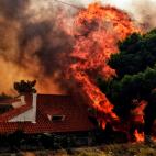 Las llamas lamen una casa de Kineta, avivadas por fuertes vientos.