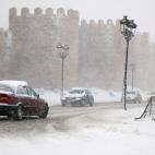 Varios veh&iacute;culos circulan por una carretera pr&oacute;xima a la muralla de &Aacute;vila que se encuentra cubierta por la nieve ca&iacute;da en las &uacute;ltimas horas.