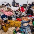 Varios refugiados se hacinan en un improvisado centro de acogida junto a sus pocas pertenencias