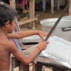 El hielo en Camboya es importante, porque es la única forma de preservar la frescura de la comida y de hacer café helado. Lo que atrae a la cámara es el tamaño del cuchillo que utiliza el niño de la imagen para cortar el hielo. La imagen es...