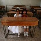 Dos chicas sentadas en un aula vacía posando para la foto mientras celebran el fin de curso en la ciudad de Duma, en Damasco.