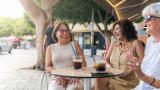 Tres mujeres sentadas en la terraza de una cafetería, disfrutando de una reunión de amigas.